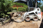 A machine moves boulders around in a yard