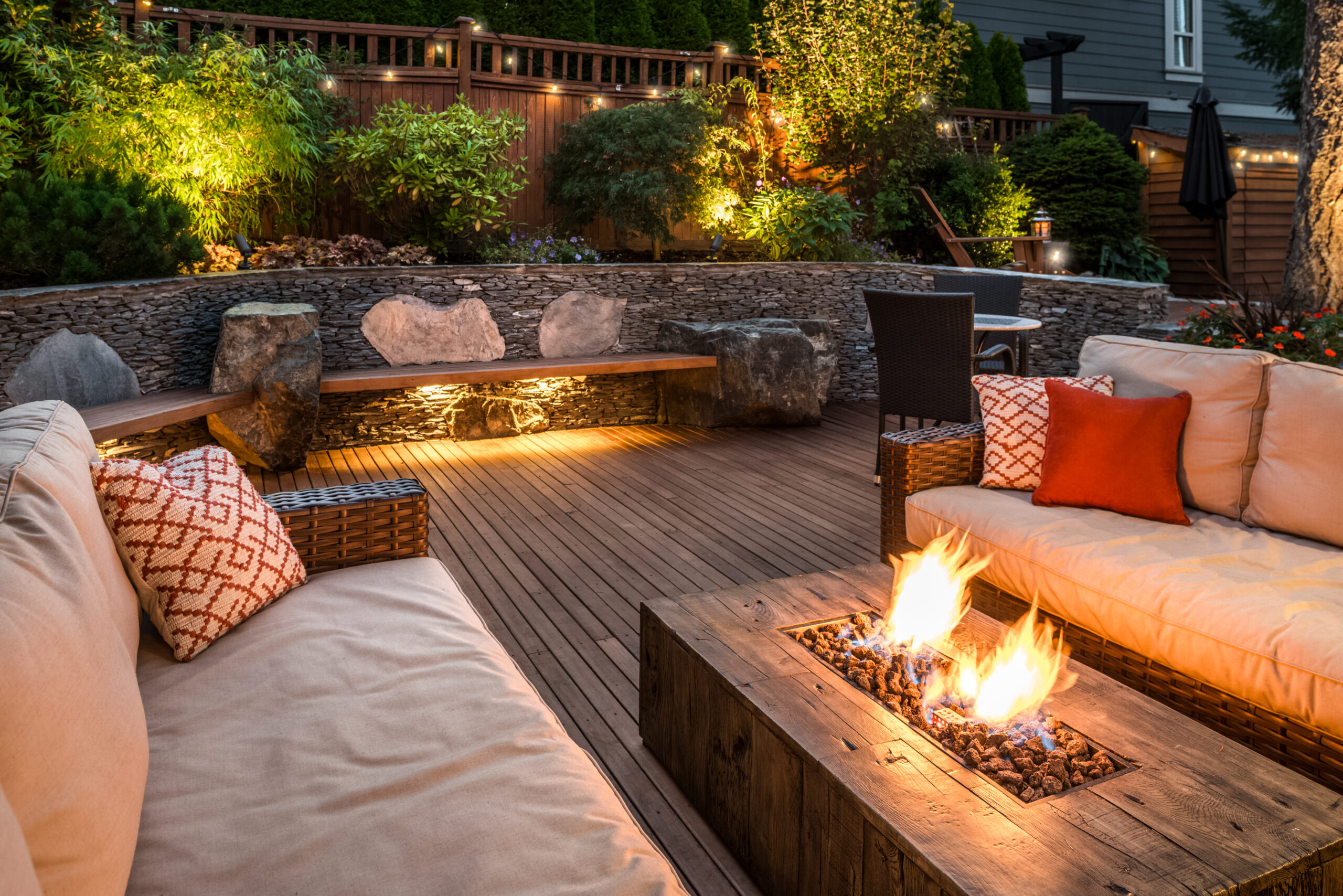 A cozy backyard retreat with a stone wall, two couches, and a fire pit