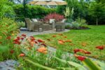 A table and chairs sit under a parasol in a lush garden